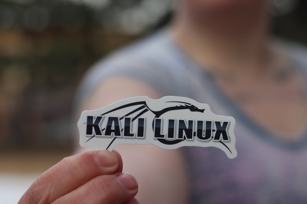 menu-02 Close-up shot of a person holding a Kali Linux sticker, highlighting cyber security themes.