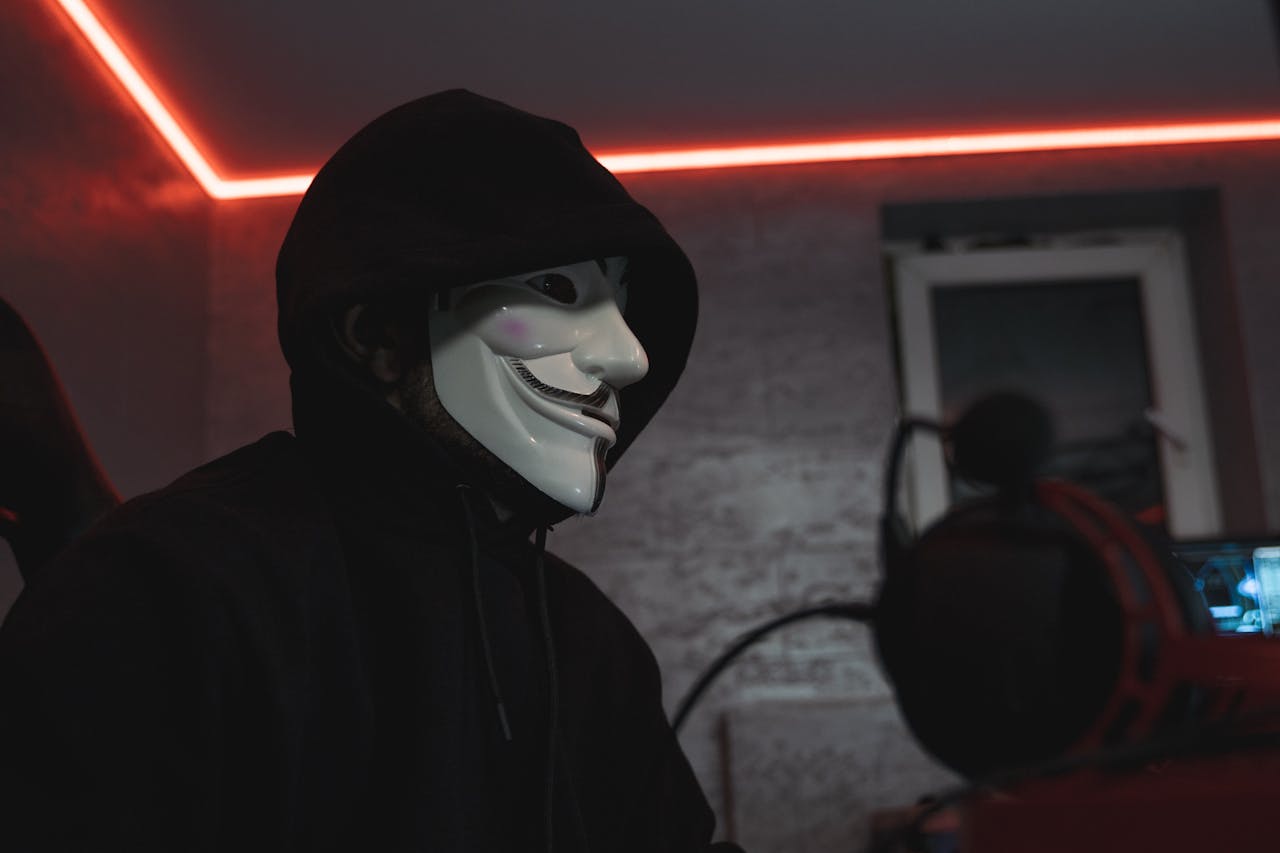 menu-12 Person wearing a hacker mask in a dimly lit room, symbolizing cyber security.