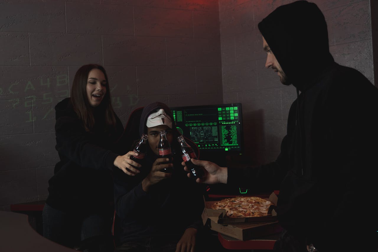menu-01 Group of hackers celebrating a successful hack with pizza and soda indoors.